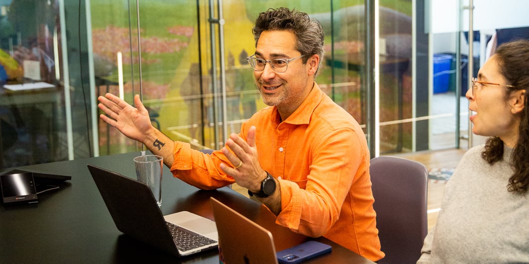 Mike Arauz sits at a conference room, smiling and gesturing with both hands as he speaks to fellow team members.